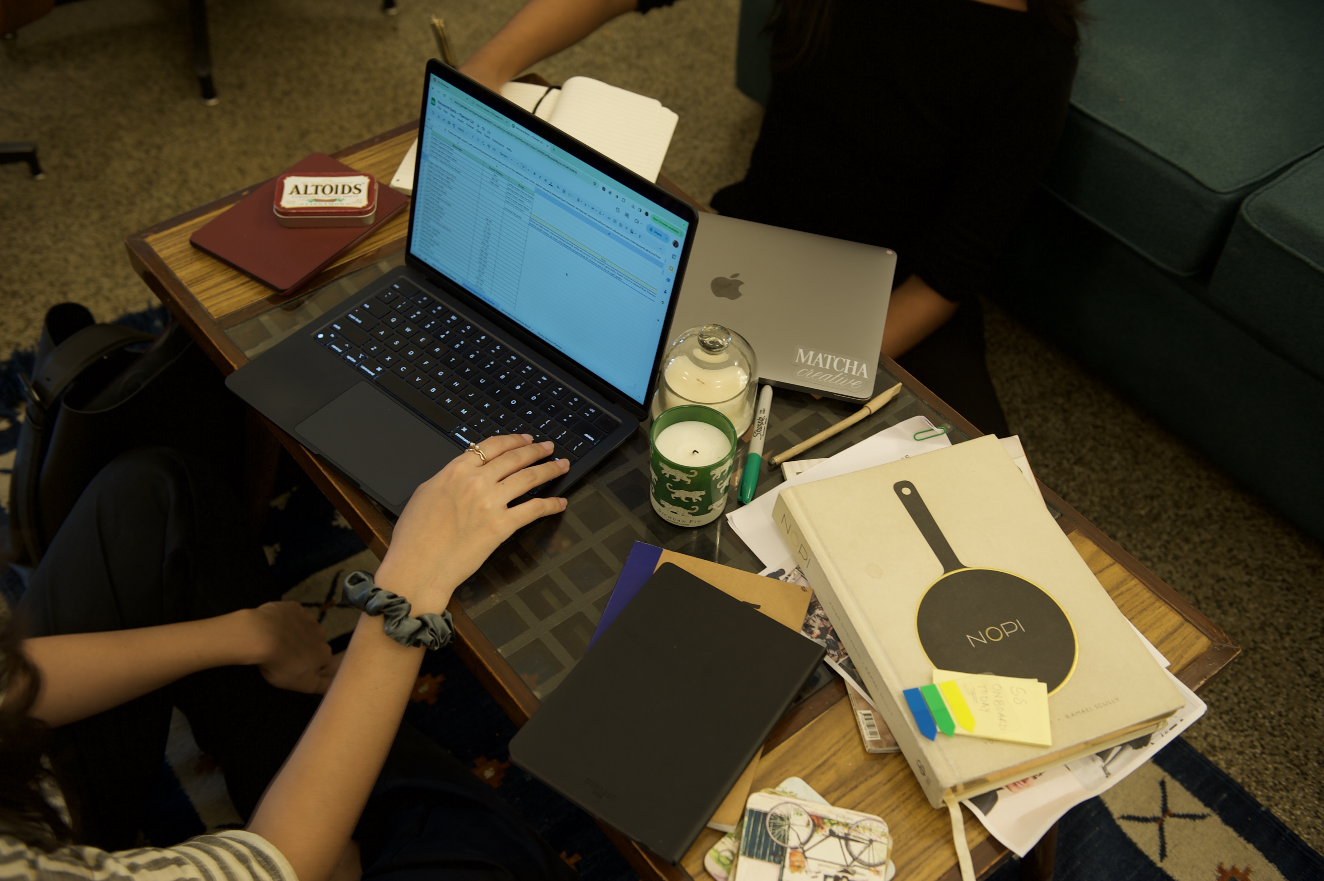 laptop on a table, one hand is working on the laptop. there are books and coasters on the table