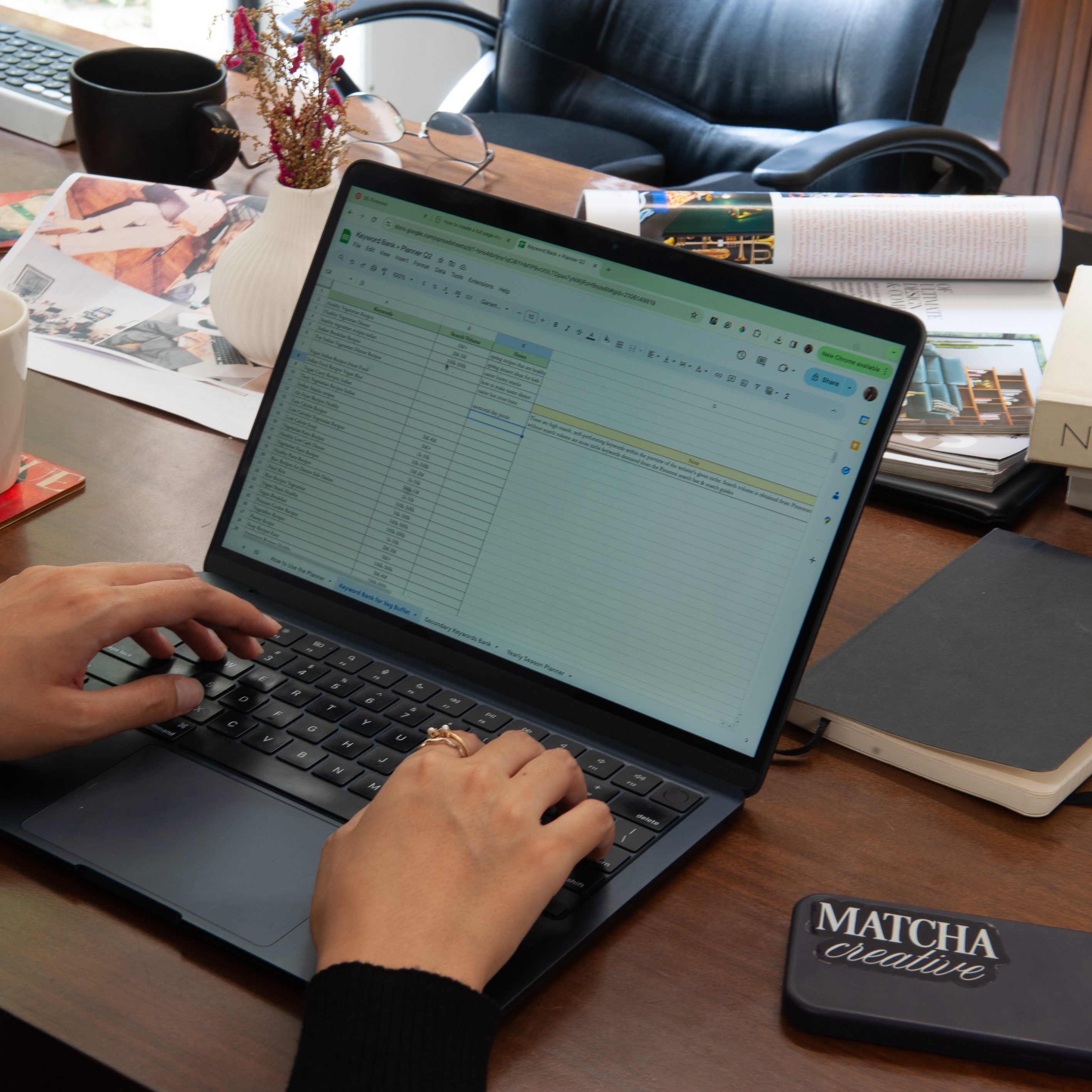 an image of a pinterest manager using her laptop to fill in a sheet on a brown desk